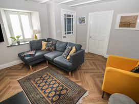 A living room with a gray sectional sofa and a yellow armchair and a patterned rug on a wood floor at Min-Y-Ffordd in Dinas Cross