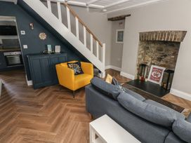 A living room with a yellow armchair a grey sofa a black cabinet under stairs and a stone fireplace at Min-Y-Ffordd in Dinas Cross