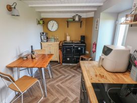 A kitchen with wooden table and chairs a stove oven countertop appliances and a clock on the wall at Min-Y-Ffordd in Dinas Cross