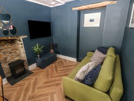 A living room with a green sofa blue walls a flat screen tv a small black stove and a wooden floor at Min-Y-Ffordd in Dinas Cross