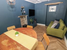 A dining area with a round wooden table and chairs next to a living space with a green sofa and wall-mounted television at Min-Y-Ffordd in Dinas Cross