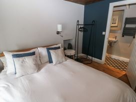 A bedroom with a double bed pillows a wall lamp a small round side table a clothes rack and a bathroom doorway at Min-Y-Ffordd in Dinas Cross