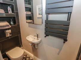 A small bathroom with a toilet sink mirror heated towel rail and wall shelves with toiletries at Min-Y-Ffordd in Dinas Cross