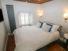 A bedroom with a double bed and pillows a window with shutters a wall mounted tv and wooden floor at Min-Y-Ffordd in Dinas Cross