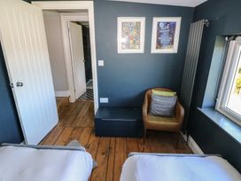 A bedroom with two single beds a wicker chair with cushions a dark blue chest and framed pictures on the wall at Min-Y-Ffordd in Dinas Cross
