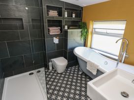 A bathroom with a shower, toilet, freestanding bathtub, sink, and shelves with towels at Min-Y-Ffordd in Dinas Cross
