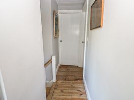A hallway with wooden floorboards two framed pictures on the walls and a white door at Min-Y-Ffordd in Dinas Cross
