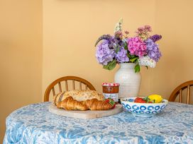 A dining table with croissants, jam, fruit bowl and flowers at Bodior Lodge in Rhoscolyn
