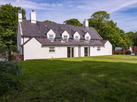 A white house with a dark roof and lawn in front surrounded by trees at Bodior Garden Cottage in Rhoscolyn