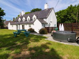 An outdoor area with a white cottage building a blue picnic table and a round hot tub in the grass at Bodior Garden Cottage in Rhoscolyn