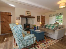 A living room with patterned armchairs a wood burning stove a sofa a coffee table and wooden doors at Bodior Garden Cottage in Rhoscolyn