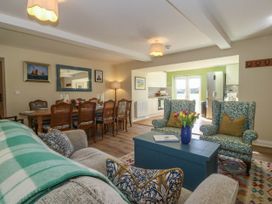 An open living and dining area with patterned armchairs a dining table and kitchen appliances at Bodior Garden Cottage in Rhoscolyn