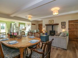 A combined dining and living room with a wooden dining table set with plates and chairs and a sitting area with sofas a stove and wooden doors at Bodior Garden Cottage in Rhoscolyn