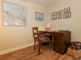 A wooden desk with a chair a lamp and framed pictures on the wall with a basket containing blankets on the floor at Bodior Garden Cottage in Rhoscolyn