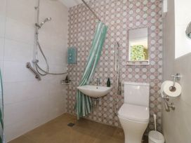 A bathroom with a shower area sink toilet mirror and striped shower curtain at Bodior Garden Cottage in Rhoscolyn