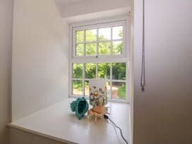 A window with a white windowsill holding two seashells and a cylindrical lamp with floral designs at Bodior Garden Cottage in Rhoscolyn