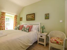 A bedroom with a double bed with striped and floral pillows a bedside table with a lamp a wicker chair with a floral cushion and floral curtains at Bodior Garden Cottage in Rhoscolyn