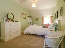 A bedroom with a bed pillows and bedside table next to a window with floral curtains at Bodior Garden Cottage in Rhoscolyn