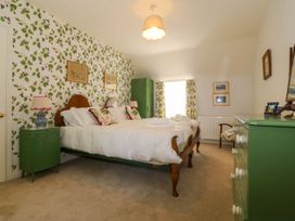 A bedroom with a double bed green bedside tables and dresser with floral wallpaper at Bodior Garden Cottage in Rhoscolyn