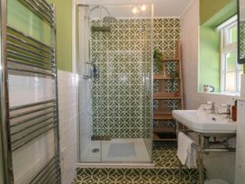 A bathroom with a glass shower enclosure and patterned green and white tiles at Bodior Garden Cottage in Rhoscolyn