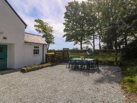 An outdoor patio area with a table and chairs next to a white house and trees at Bodior Garden Cottage in Rhoscolyn