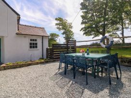 An outdoor patio with a table and six chairs next to a white house at Bodior Garden Cottage in Rhoscolyn