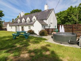 A white cottage with multiple windows and chimneys a green picnic table and a round hot tub in the garden at Bodior Garden Cottage in Rhoscolyn