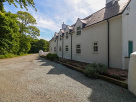 A white house with multiple windows and a gravel driveway next to a tree-lined road at Bodior Garden Cottage in Rhoscolyn