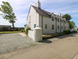 An exterior view of a white two-story house with multiple windows next to a gravel driveway and a fenced garden area at Bodior Garden Cottage in Rhoscolyn