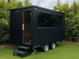 A black cabin structure with large windows and steps at Green Shutters near Freshwater East