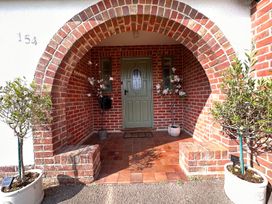 A brick arched porch with a green front door and potted plants on either side at Bayview Cottage in Southbourne