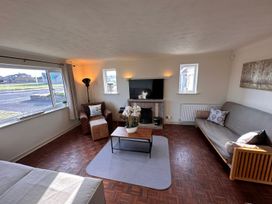 A living room with a coffee table and flower pot in the center a tv on the wall a brown armchair and a gray sofa at Bayview Cottage in Southbourne