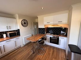 A kitchen with wood countertops black tiled backsplash a small dining table with two stools and a microwave at Bayview Cottage in Southbourne