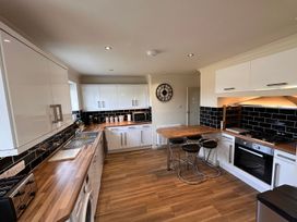 A kitchen with wooden countertops white cabinets black tiled backsplash and a breakfast bar with stools at Bayview Cottage in Southbourne