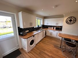 A kitchen with white cabinets wooden countertops a washing machine a toaster microwave and stools at Bayview Cottage in Southbourne