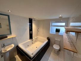 A bathroom with a bathtub shower toilet sink mirror and wooden shelves at Bayview Cottage in Southbourne
