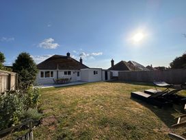 A backyard with a lawn table and chairs near a house and lounge chairs on the grass at Bayview Cottage in Southbourne