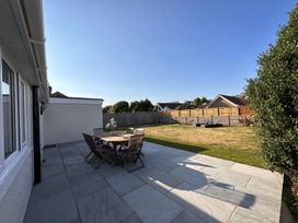 An outdoor patio with a wooden dining table and chairs next to a grassy backyard with a hammock and lounge chairs at Bayview Cottage in Southbourne
