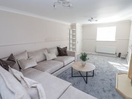 A living room with a large sofa a round wooden coffee table a small shelving unit and a window at 9 Beckett Close in Colwyn Bay