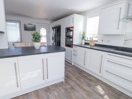 A kitchen with white cabinets, black countertops, a double oven, a refrigerator, a vase with green foliage on the island at 9 Beckett Close in Colwyn Bay
