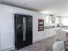 A kitchen with white cabinets a black double door refrigerator a red double oven and light colored chairs at 9 Beckett Close in Colwyn Bay