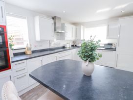 A kitchen with white cabinets black countertops a vase with green leaves on a central island and appliances at 9 Beckett Close in Colwyn Bay