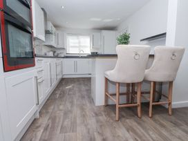 A kitchen with white cabinets two beige bar stools and wood flooring at 9 Beckett Close in Colwyn Bay