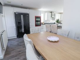 A kitchen with a black double door refrigerator white cabinets a wooden dining table with beige upholstered chairs and a countertop with stools at 9 Beckett Close Colwyn Bay