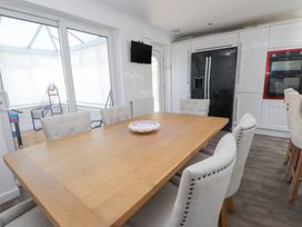 A dining area with a wooden table and upholstered chairs next to a kitchen with a black refrigerator and white cabinets at 9 Beckett Close in Colwyn Bay