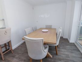 A dining room with a wooden table surrounded by six upholstered chairs and a serving dish on the table at 9 Beckett Close in Colwyn Bay
