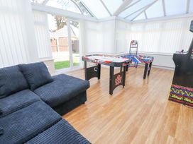 A conservatory with a black sectional sofa an air hockey table a foosball table and a video arcade machine at 9 Beckett Close in Colwyn Bay