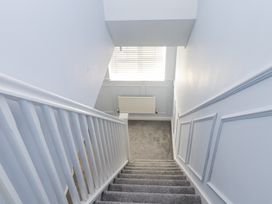 A carpeted staircase with white railing leading down to a landing with a radiator and window blinds at 9 Beckett Close in Colwyn Bay