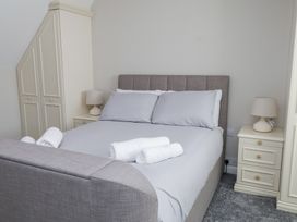 A bedroom with a grey upholstered bed with pillows and rolled towels on top and bedside tables with lamps at 9 Beckett Close in Colwyn Bay