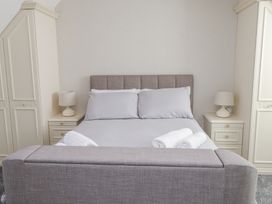 A bedroom with a grey upholstered bed two white bedside tables with lamps and built in wardrobes at 9 Beckett Close in Colwyn Bay